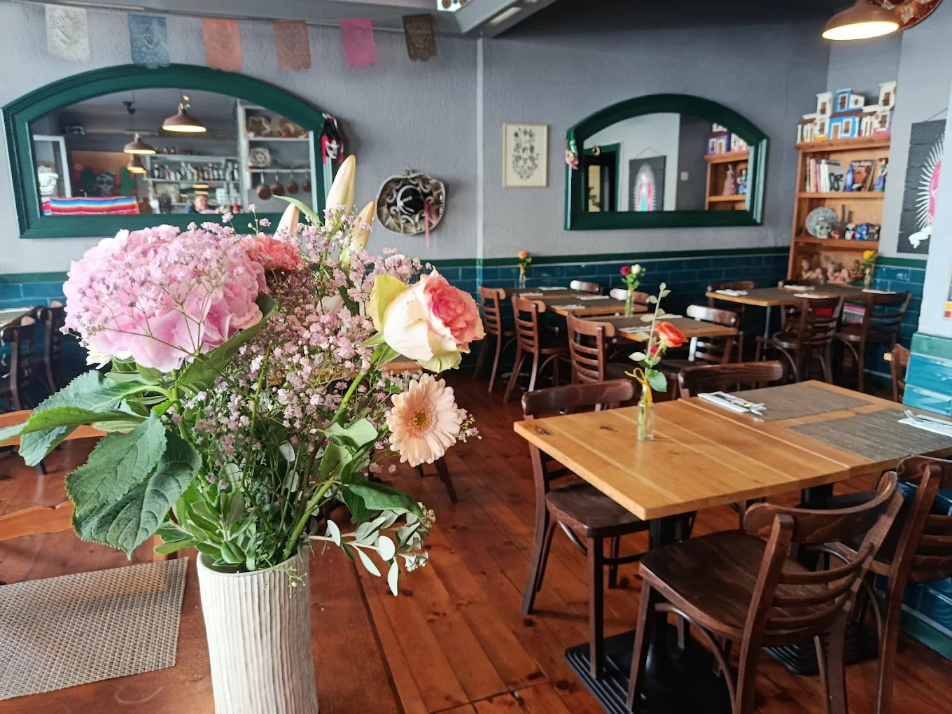 Salle chaleureuse du Mexicain : bouquet de fleurs, soubassement carrelé vert et tables en bois.